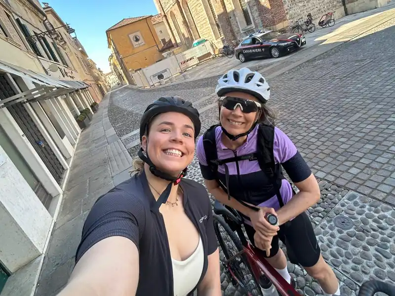 Two smiling riders taking a selfie on a cobbled street in an old town